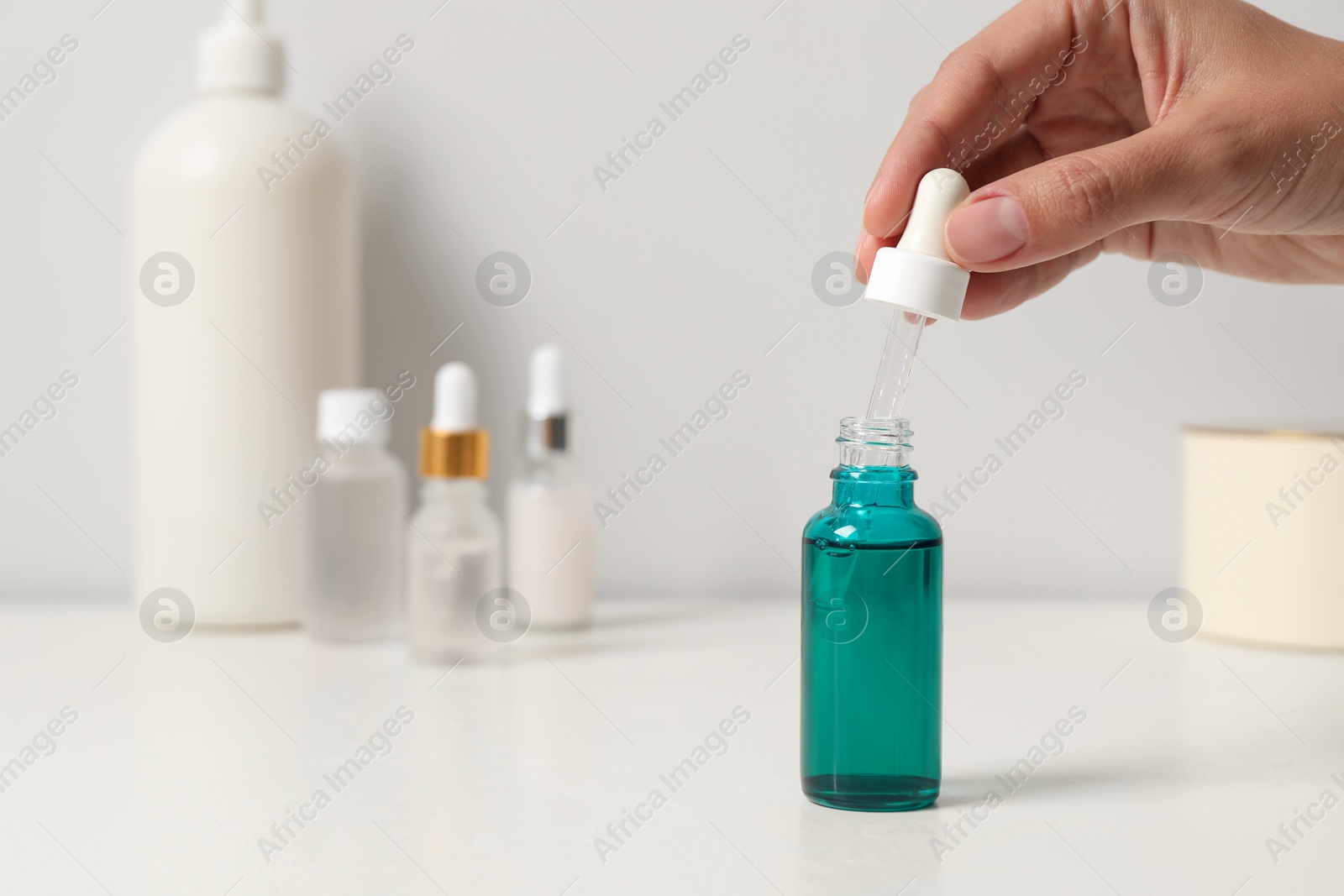 Photo of Woman with cosmetic serum at white table, closeup. Space for text