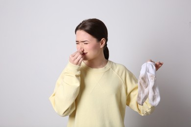 Young woman feeling bad smell from dirty socks on light grey background