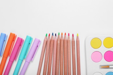 Photo of Watercolor palette, colorful pencils and markers on white background, flat lay. Space for text