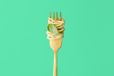 Fork with tasty pasta and basil on green background