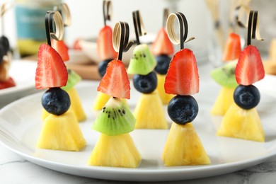 Photo of Tasty canapes with pineapple, kiwi and berries on white marble table, closeup