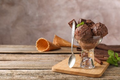 Tasty chocolate ice cream in glass dessert bowl served on wooden table. Space for text