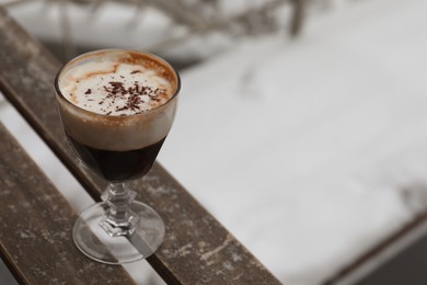 Glass of aromatic coffee with chocolate powder on wooden bench outdoors in winter, space for text