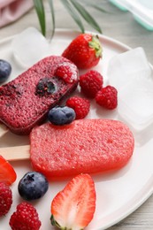 Photo of Plate of tasty berry ice pops on white wooden table, closeup. Fruit popsicle
