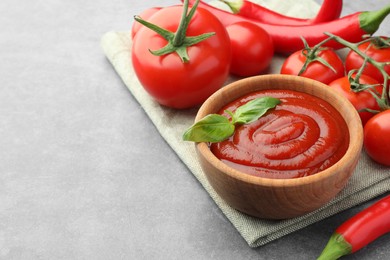 Photo of Bowl of tasty ketchup and ingredients on light grey table, closeup. Space for text