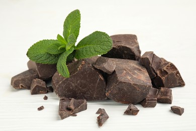 Photo of Tasty dark chocolate pieces with mint on white wooden table, closeup