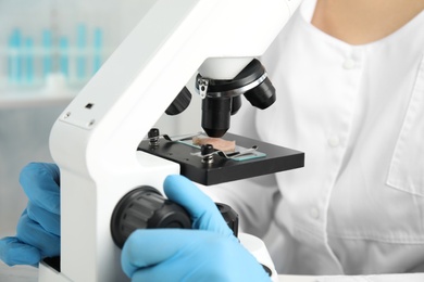 Photo of Scientist inspecting meat sample with microscope in laboratory, closeup. Poison detection