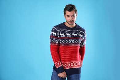 Photo of Portrait of happy young man in Christmas sweater on light blue background