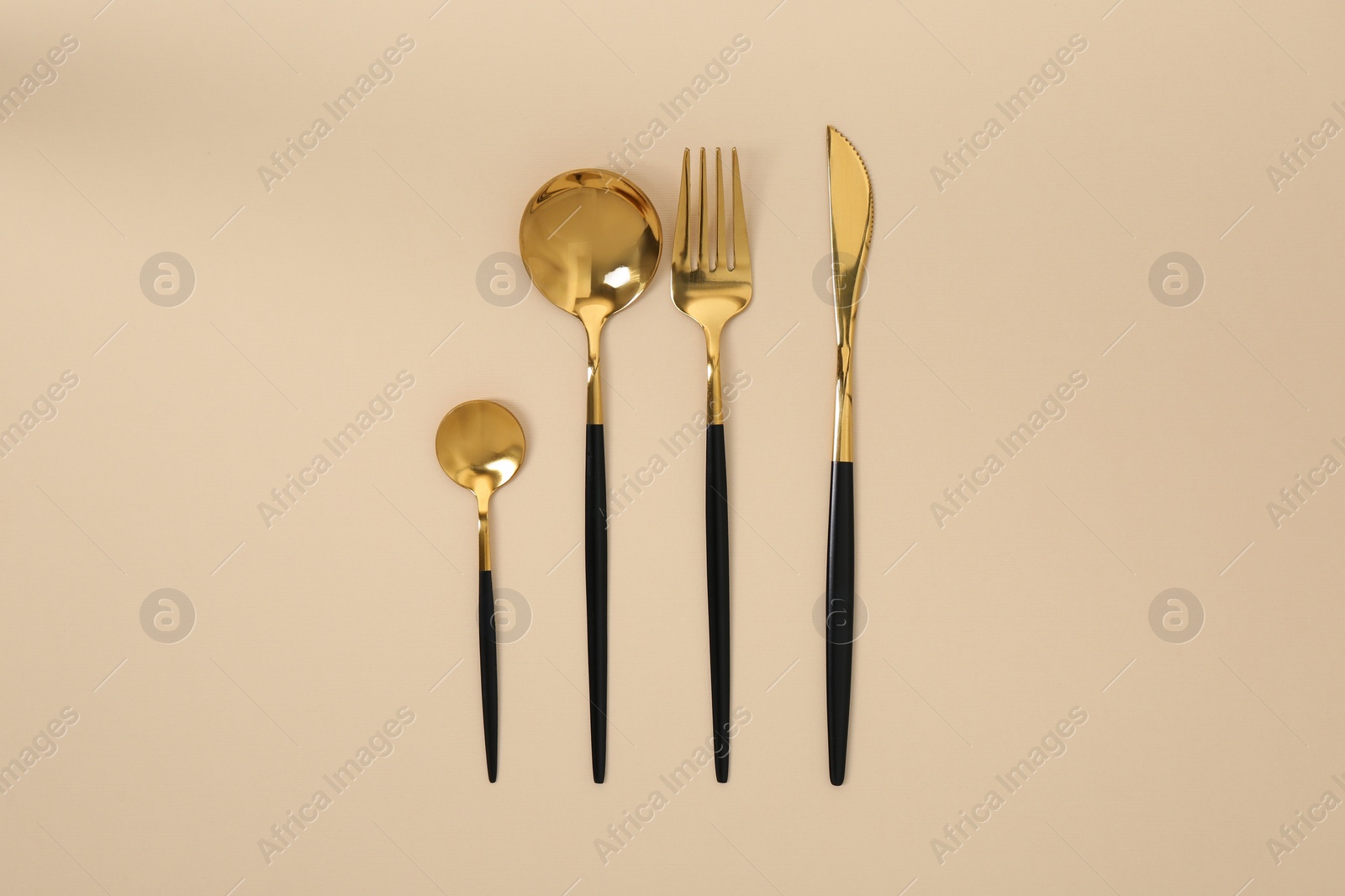 Photo of Stylish golden cutlery set on beige background, flat lay