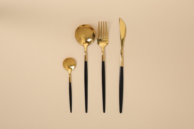 Stylish golden cutlery set on beige background, flat lay