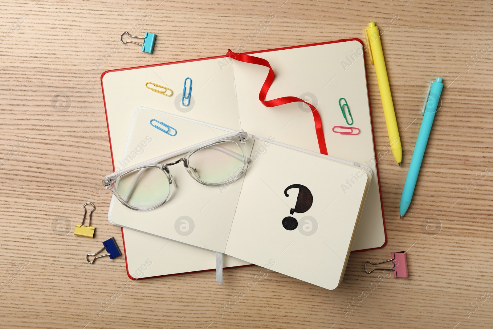 Photo of Notebook with question mark and stationery on wooden table, flat lay