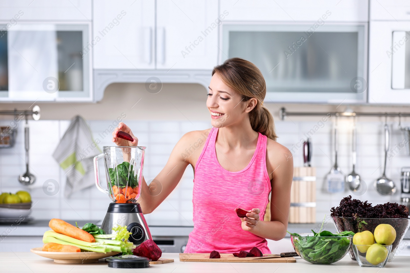 Photo of Young woman preparing tasty healthy smoothie at table in kitchen