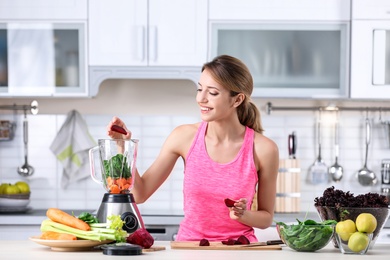 Young woman preparing tasty healthy smoothie at table in kitchen