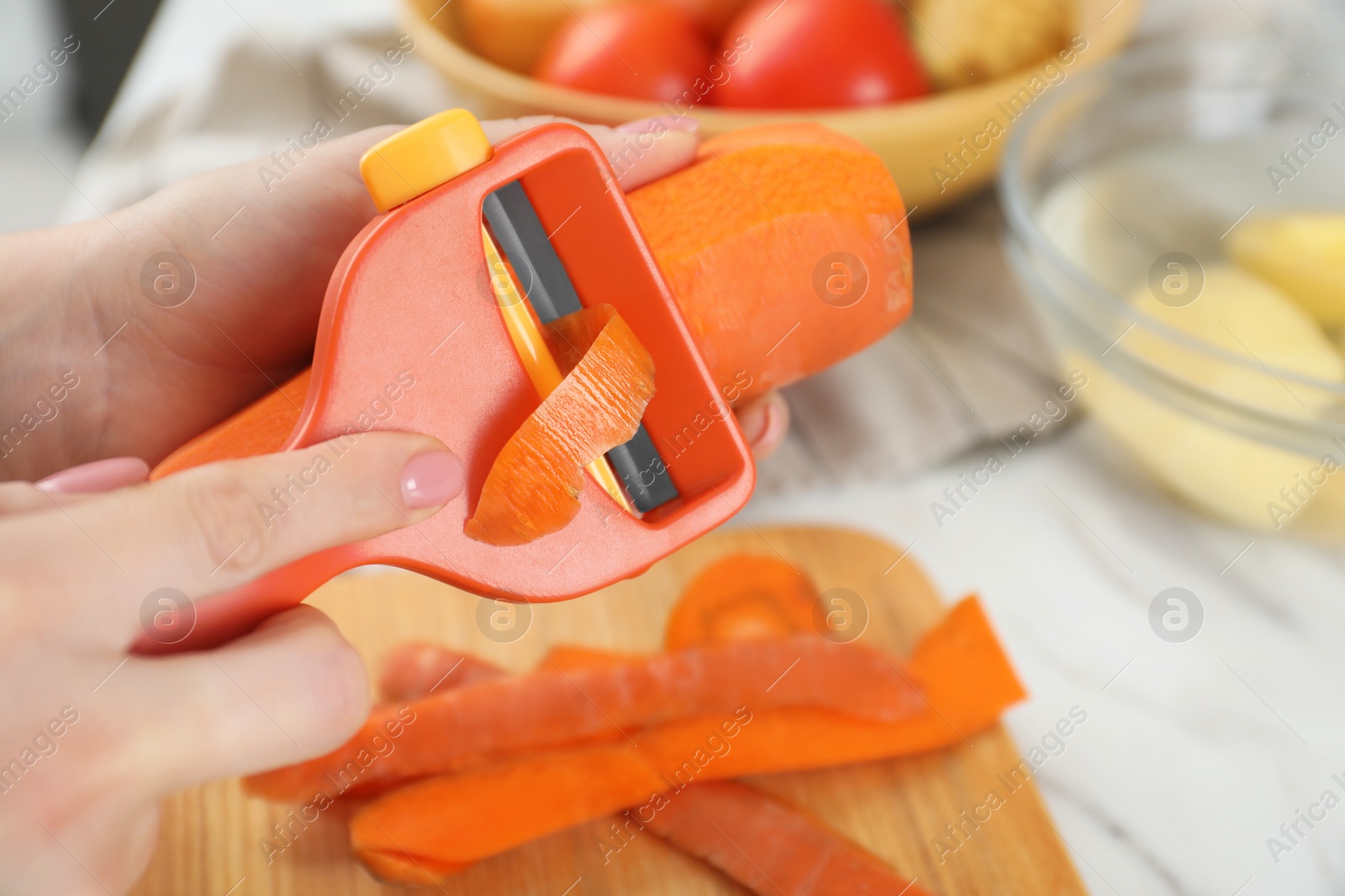 Photo of Woman peeling fresh carrot at white marble table, closeup