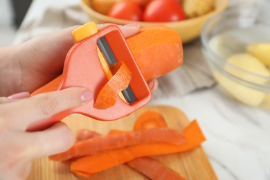 Photo of Woman peeling fresh carrot at white marble table, closeup