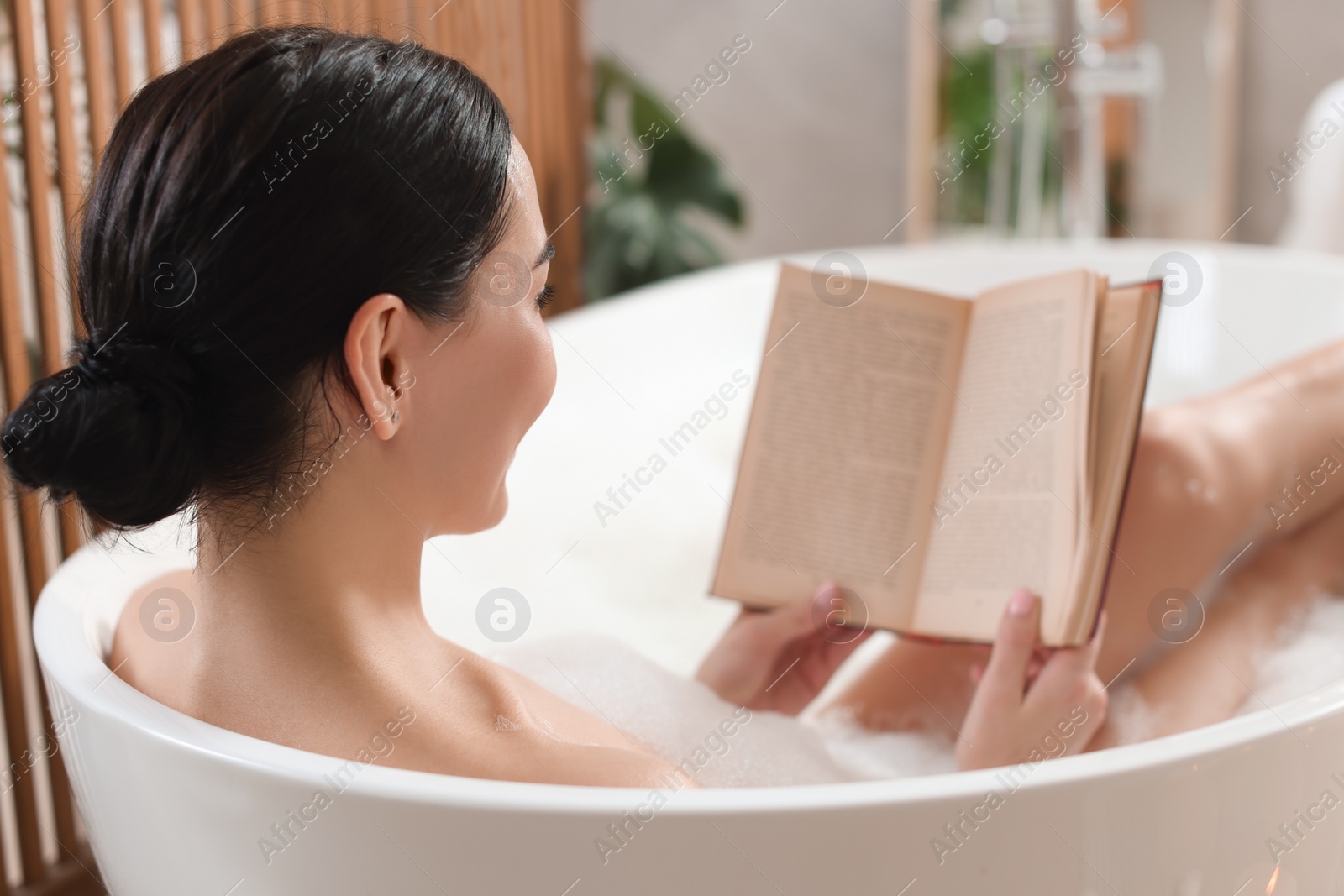 Photo of Beautiful young woman reading book while taking bath at home