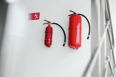 Photo of Fire extinguishers and emergency exit sign on white wall indoors