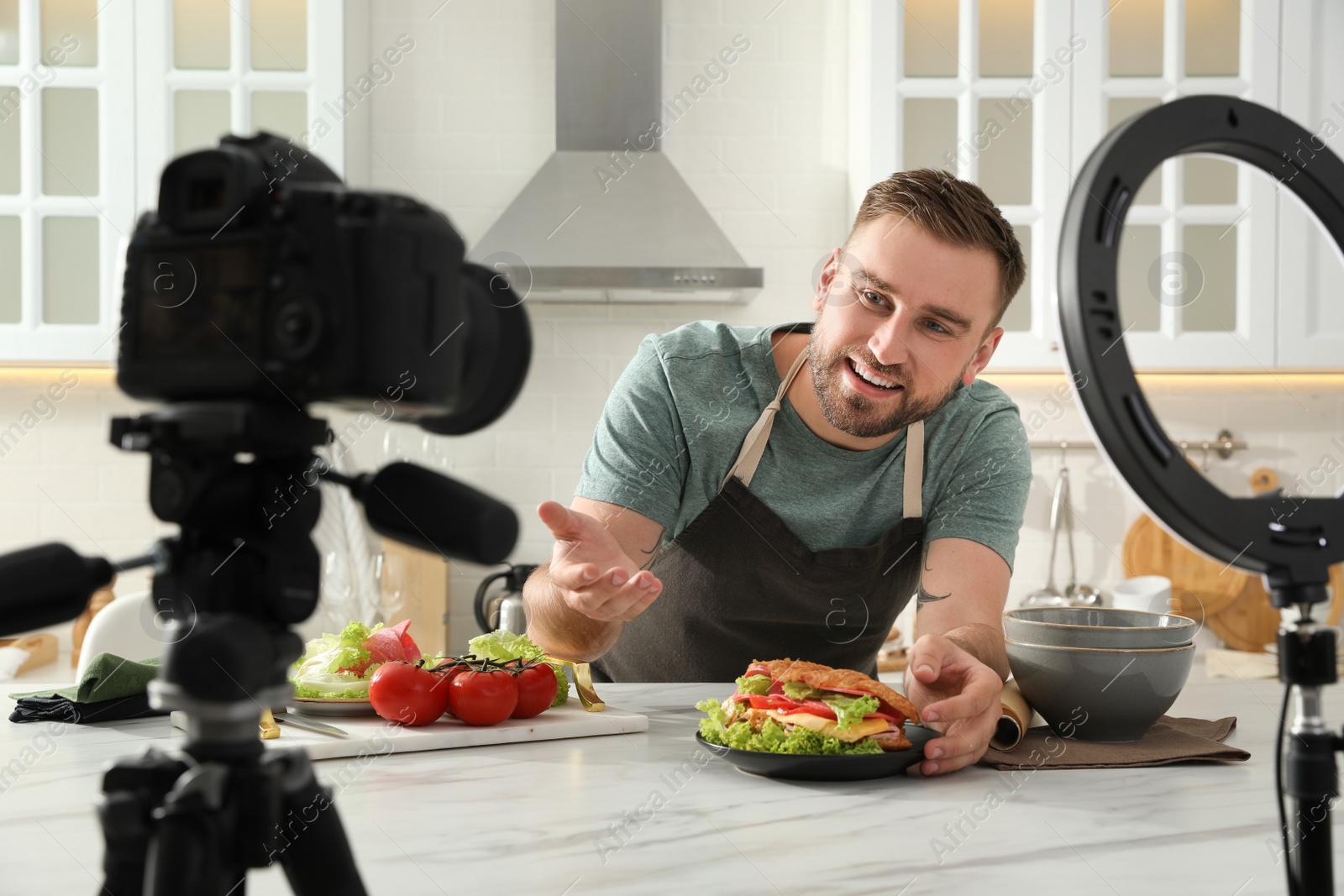 Photo of Blogger with tasty croissant recording video in kitchen at home. Using ring lamp and camera