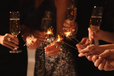 Friends with glasses of sparkling wine and sparklers celebrating New Year, closeup