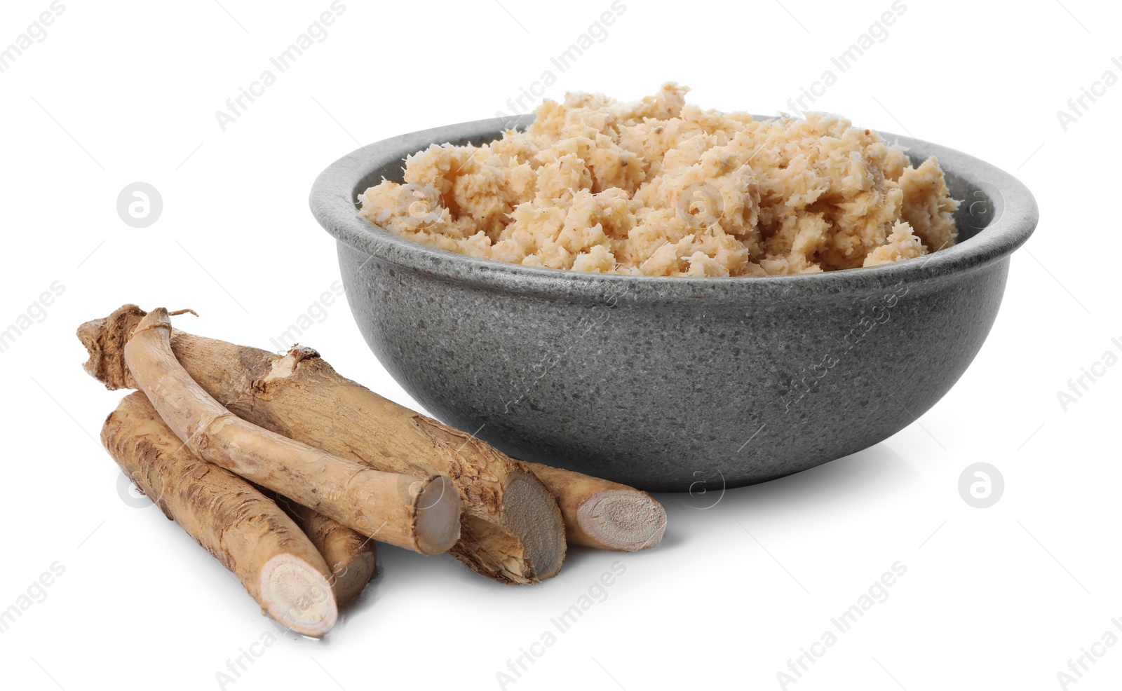 Photo of Bowl of tasty prepared horseradish and roots isolated on white