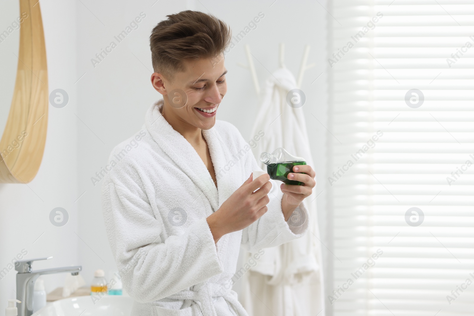 Photo of Young man using mouthwash in bathroom. Oral hygiene