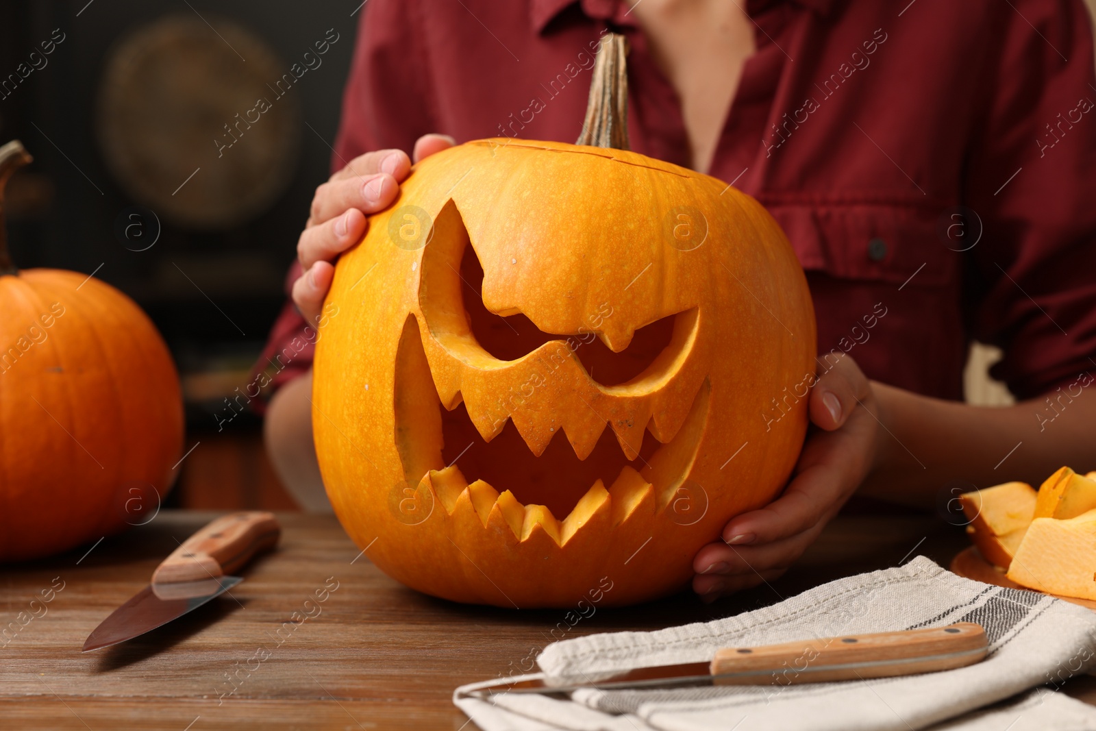 Photo of Woman holding carved pumpkin for Halloween at wooden table, closeup