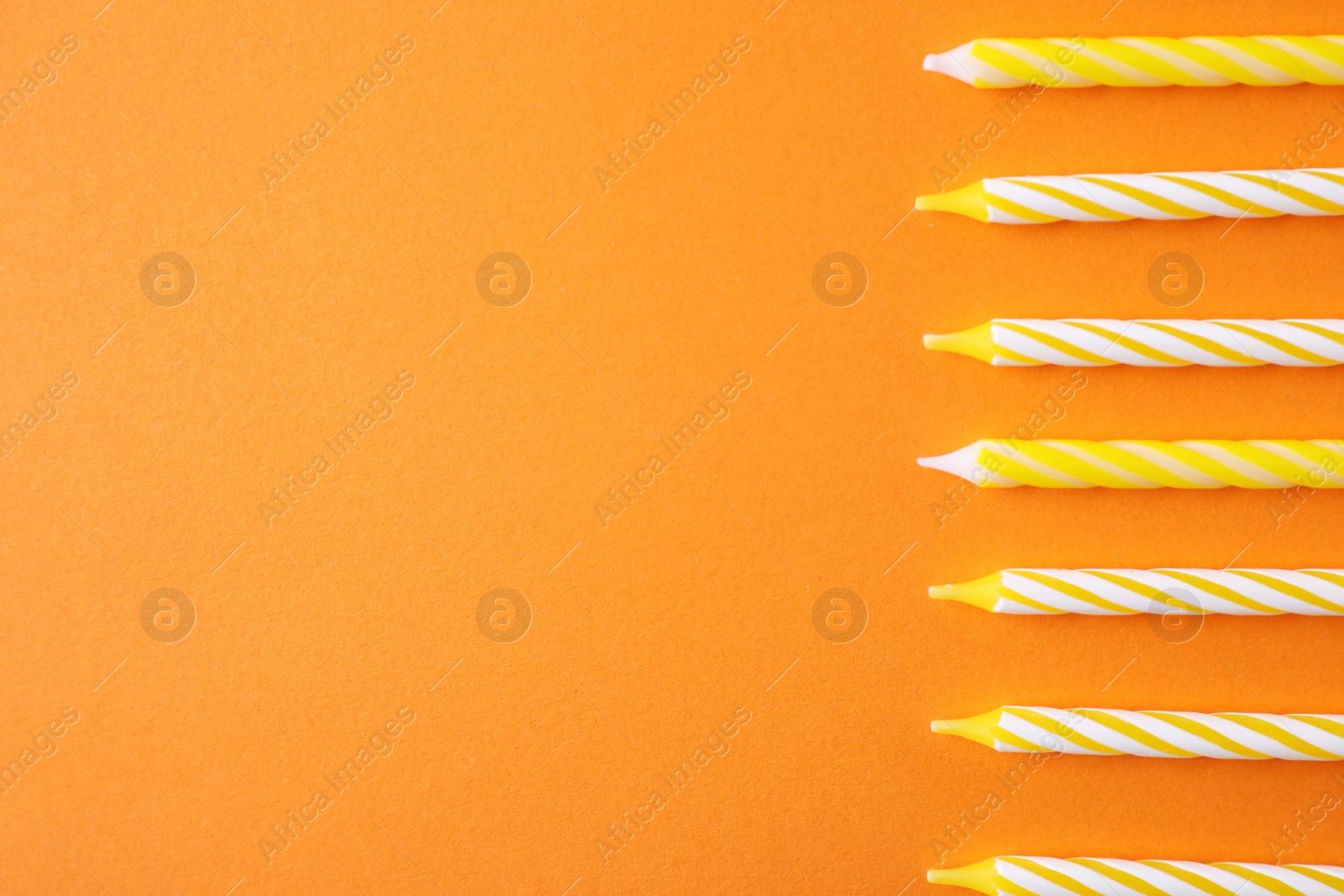 Photo of Colorful striped birthday candles on orange background, top view with space for text