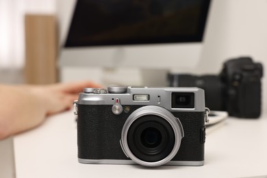 Photographer working on computer at white table with camera indoors, closeup