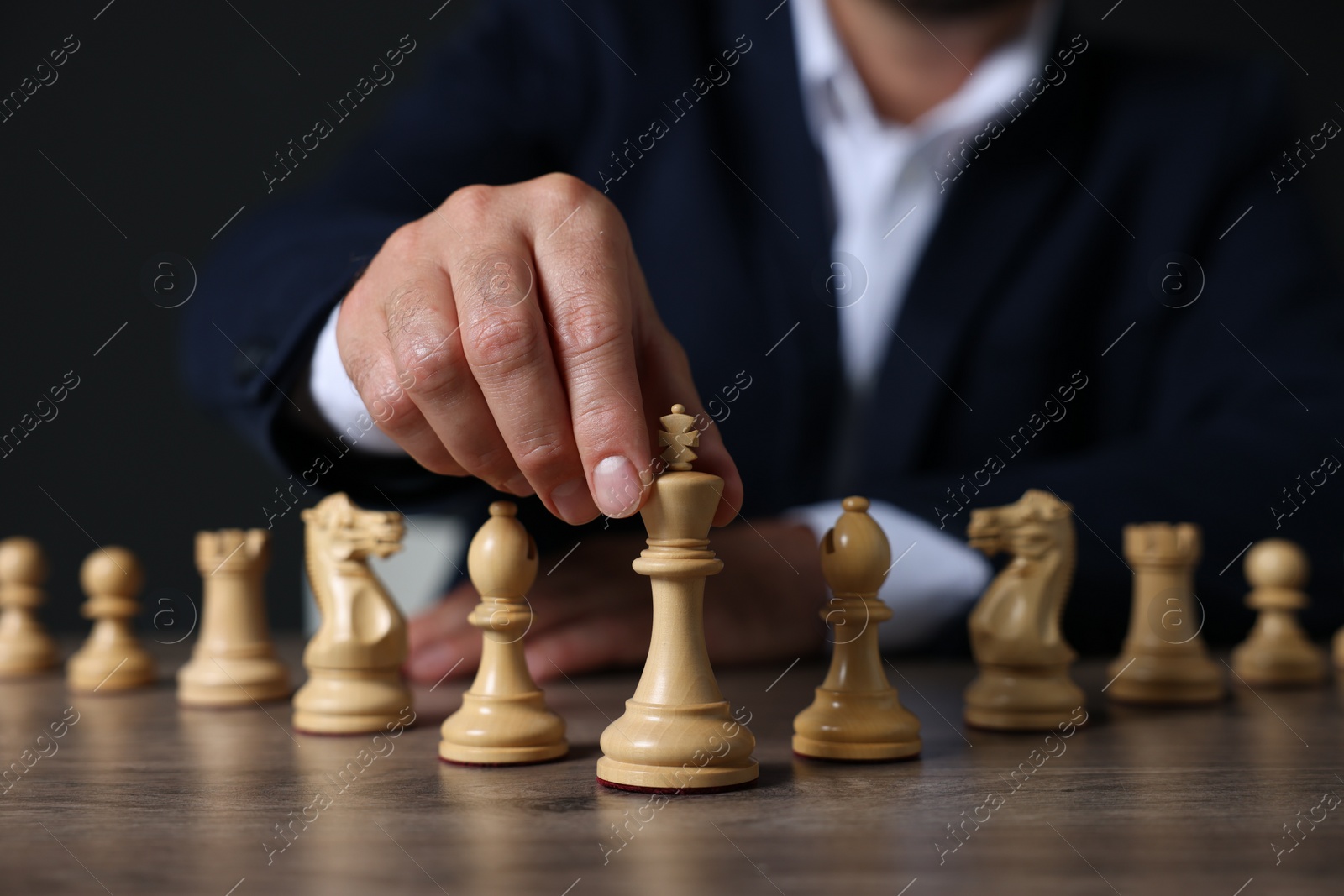 Photo of Man with chess pieces at wooden table against dark background, closeup