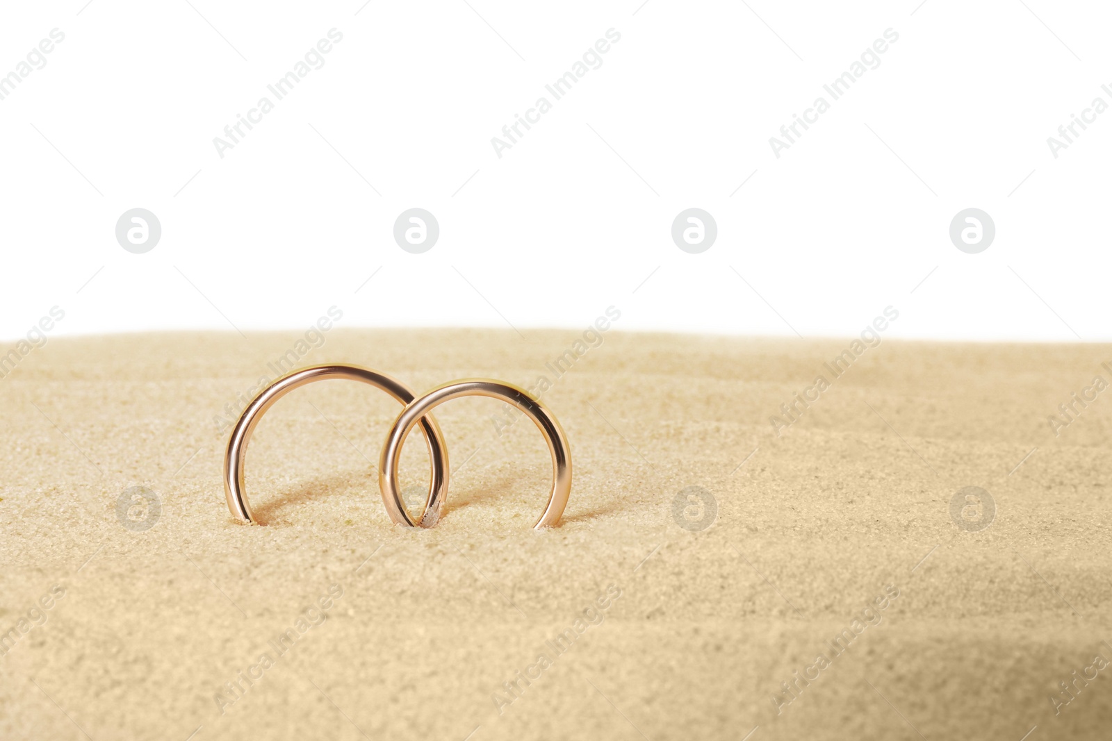 Photo of Honeymoon concept. Two golden rings and sand isolated on white