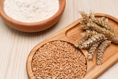 Photo of Wheat grains, flour and spikelets on wooden table, closeup