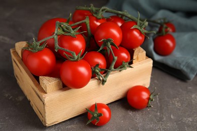 Photo of Many ripe red tomatoes in wooden crate on grey table