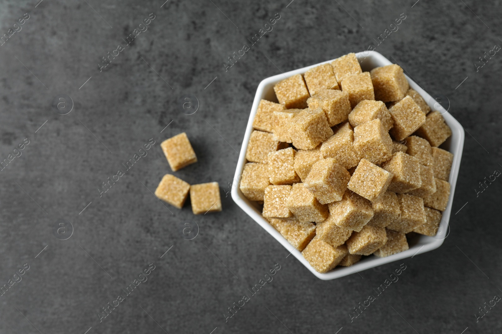 Photo of Brown sugar cubes in bowl on grey table, top view. Space for text