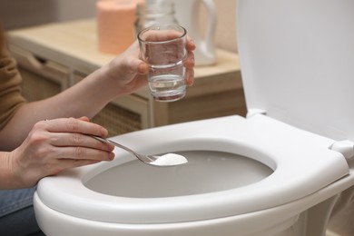 Photo of Woman cleaning toilet bowl with baking soda, indoors closeup