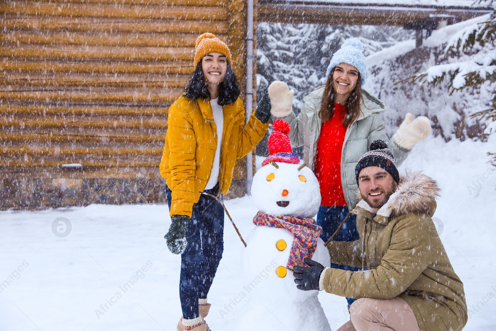 Photo of Happy friends with snowman outdoors on snowy day. Winter vacation