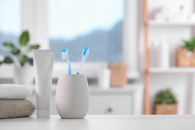 Plastic toothbrushes in holder, toothpaste and towels on white table indoors. Space for text