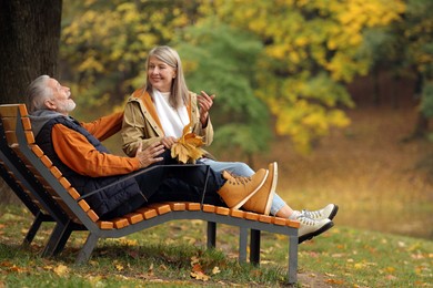 Photo of Affectionate senior couple with dry leaves spending time together in autumn park