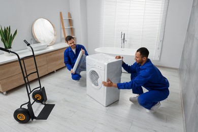 Male movers with stretch film wrapping washing machine in bathroom. New house