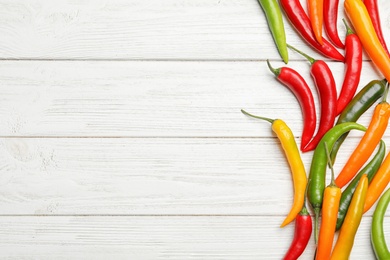 Photo of Different hot chili peppers on white wooden table, flat lay. Space for text