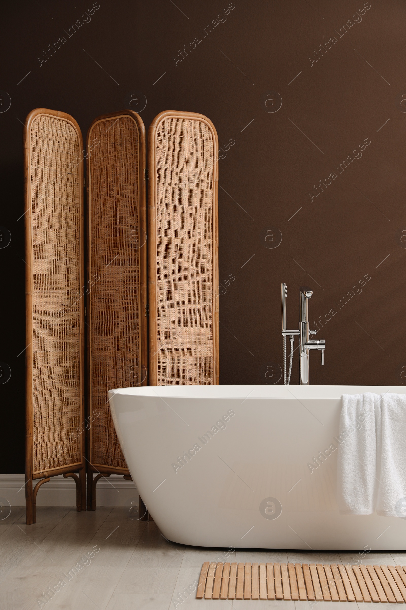 Photo of Modern ceramic bathtub and folding screen near brown wall in room