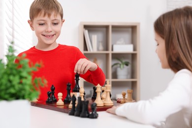 Photo of Cute children playing chess at table in room