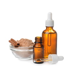 Photo of Bottles with cinnamon oil, powder and sticks on white background