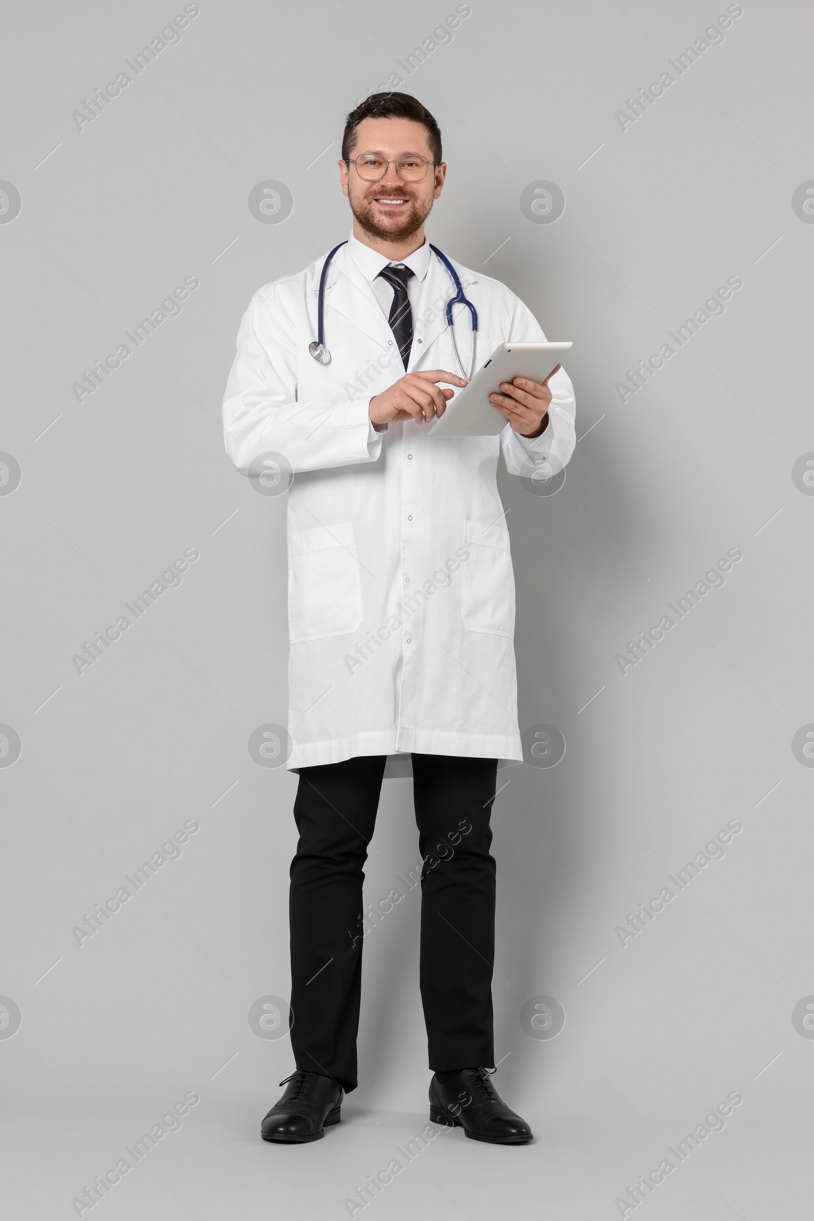 Photo of Full length portrait of smiling doctor with tablet on light grey background