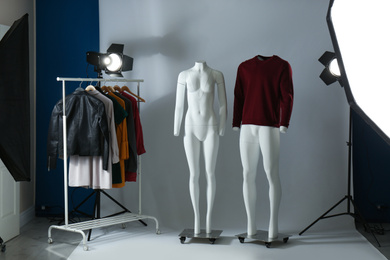 Photo of Ghost mannequins, clothes and professional lighting equipment in modern photo studio
