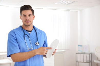 Photo of Handsome male orthopedist showing insole in clinic