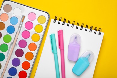 Photo of Watercolor palette, notebook and colorful markers on yellow background, flat lay