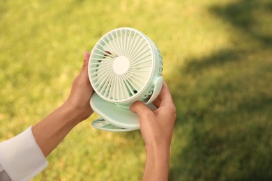 Woman holding portable fan outdoors on sunny summer day, closeup. Space for text