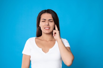 Young woman suffering from ear pain on light blue background