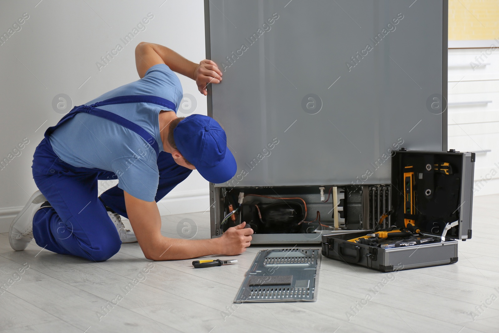 Photo of Male technician with screwdriver repairing refrigerator indoors