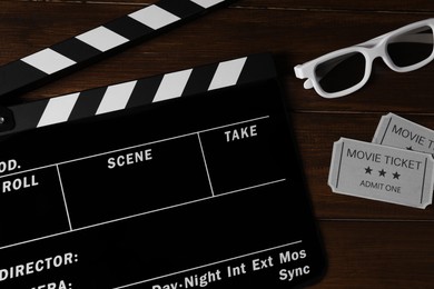 Clapperboard, movie tickets and 3D glasses on wooden table, flat lay